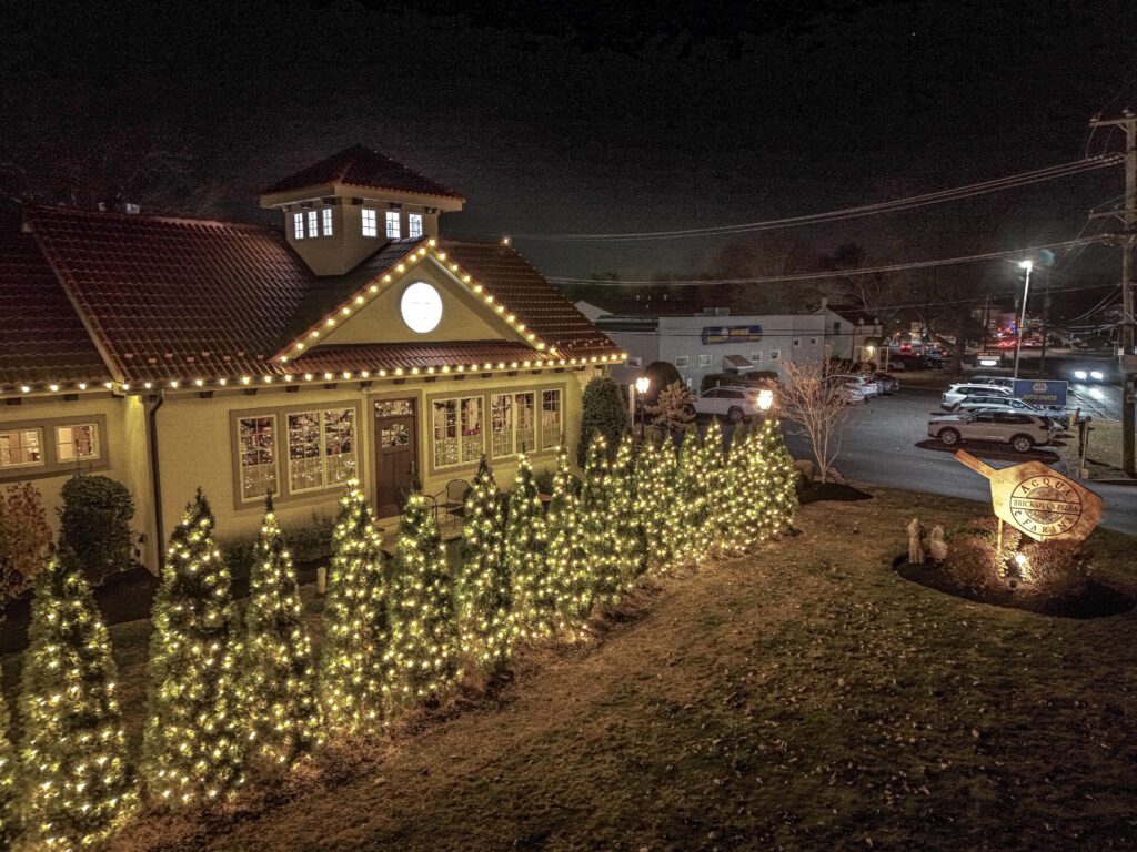 Restaurant building decorated with string lights and illuminated evergreen trees in the front yard, captured at night.