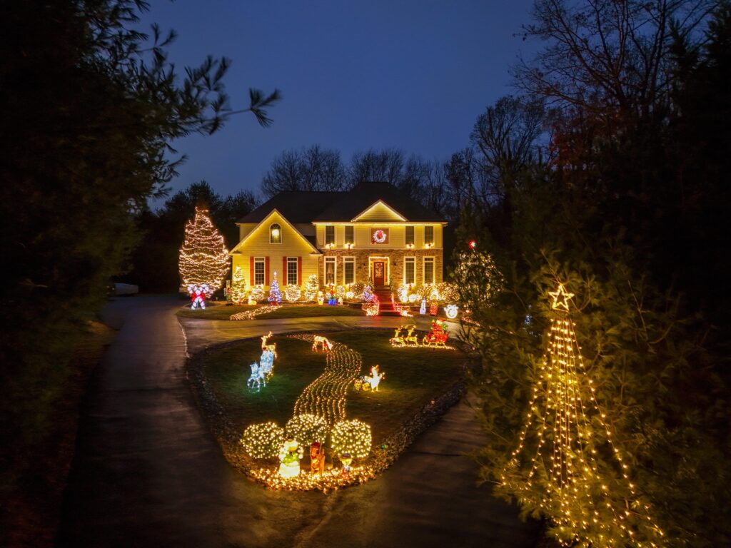 House decorated with bright Christmas lights, including trees and festive lawn ornaments, captured during the evening.